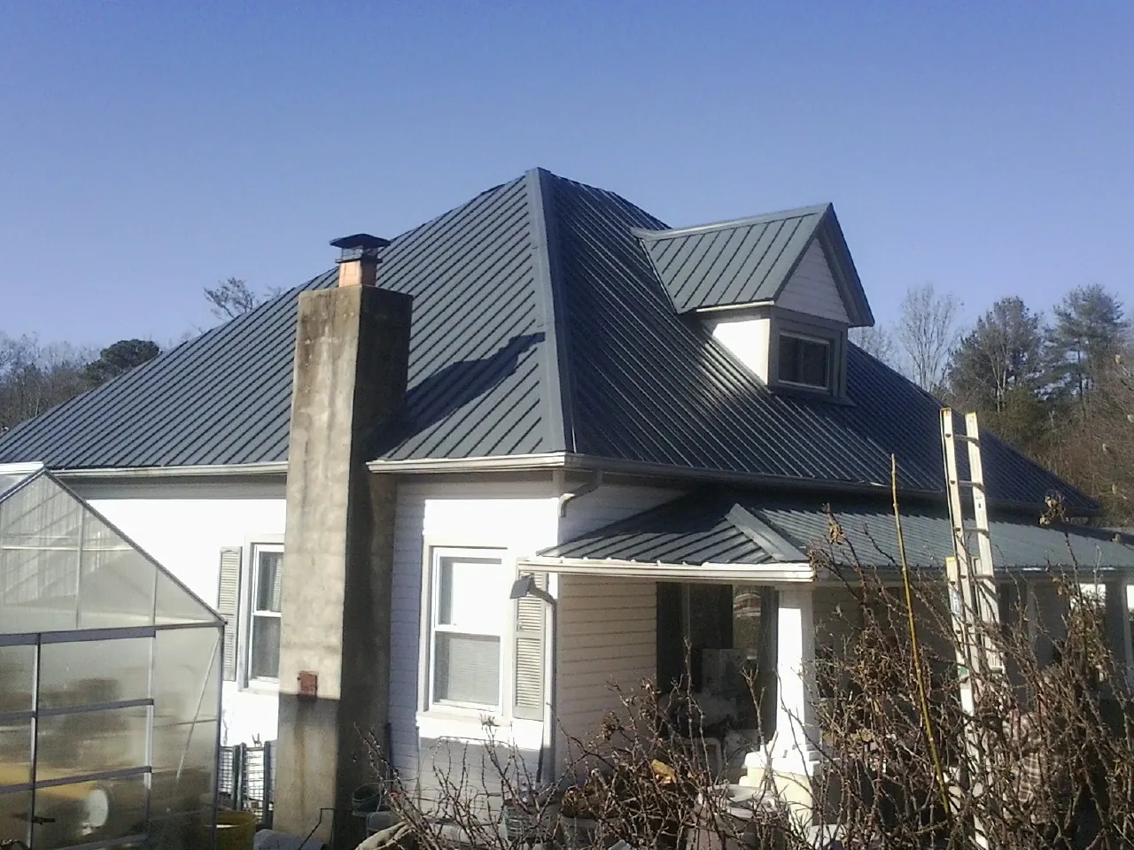 Dark blue standing seam metal roof on a white farmhouse with dormer — Slate & Tile Roof Repair by Roofing Brothers in Valley View