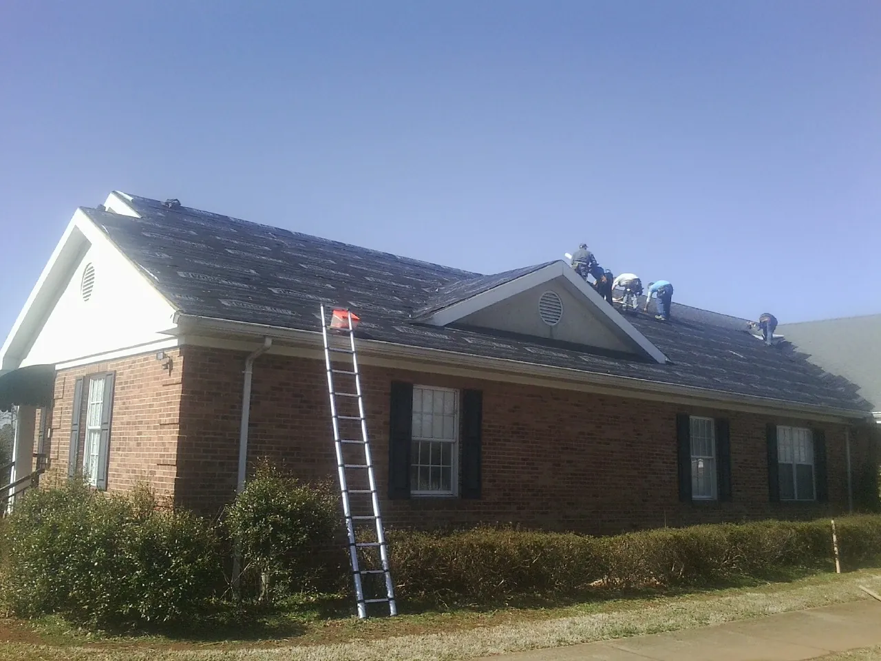 Crew tearing shingles off a brick ranch roof with a ladder set — Metal Roof Repair work by our crew in Valley View