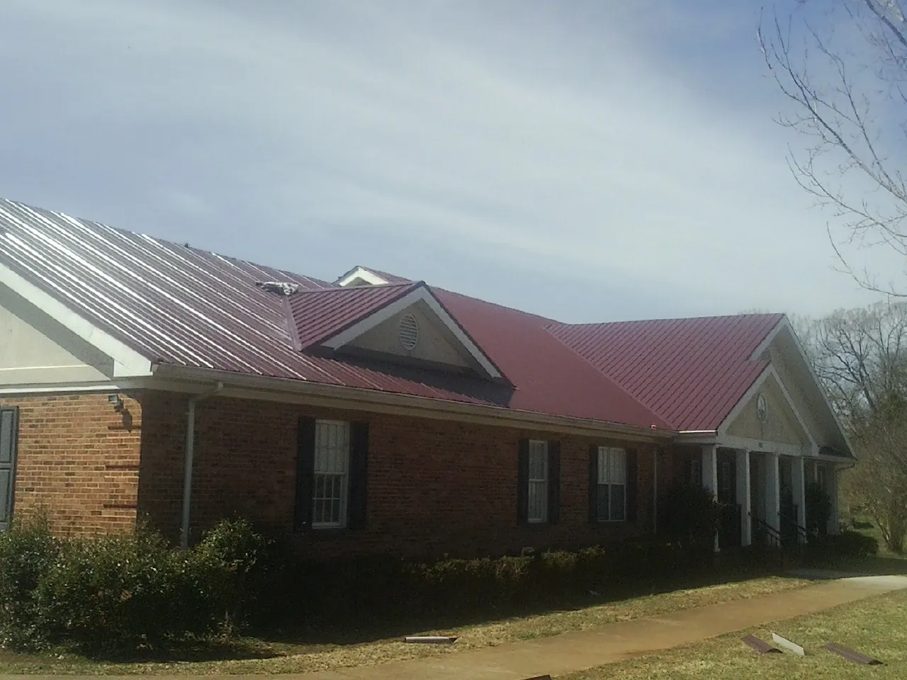 Red metal roof with gabled entries on a long brick building, from a Hail Damage Roof Repair job in Valley View