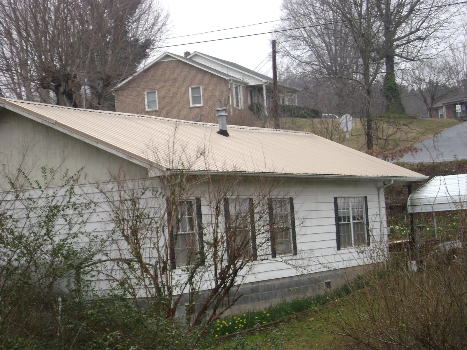 Tan metal roof on a white sided house set into a hillside — Commercial Roofing by Roofing Brothers in Valley View